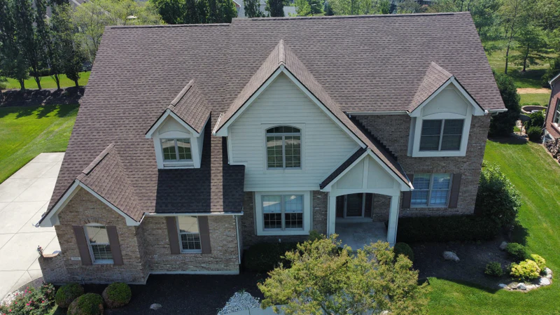 Drone view of a brick two-story home with a new weathered-wood architectural shingle roof