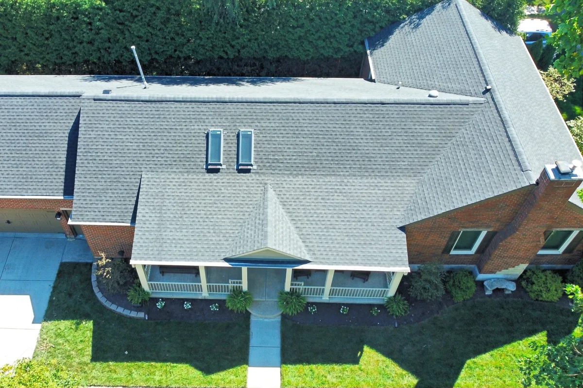 Drone view of a ranch home with a new light gray shingle roof and a skylight