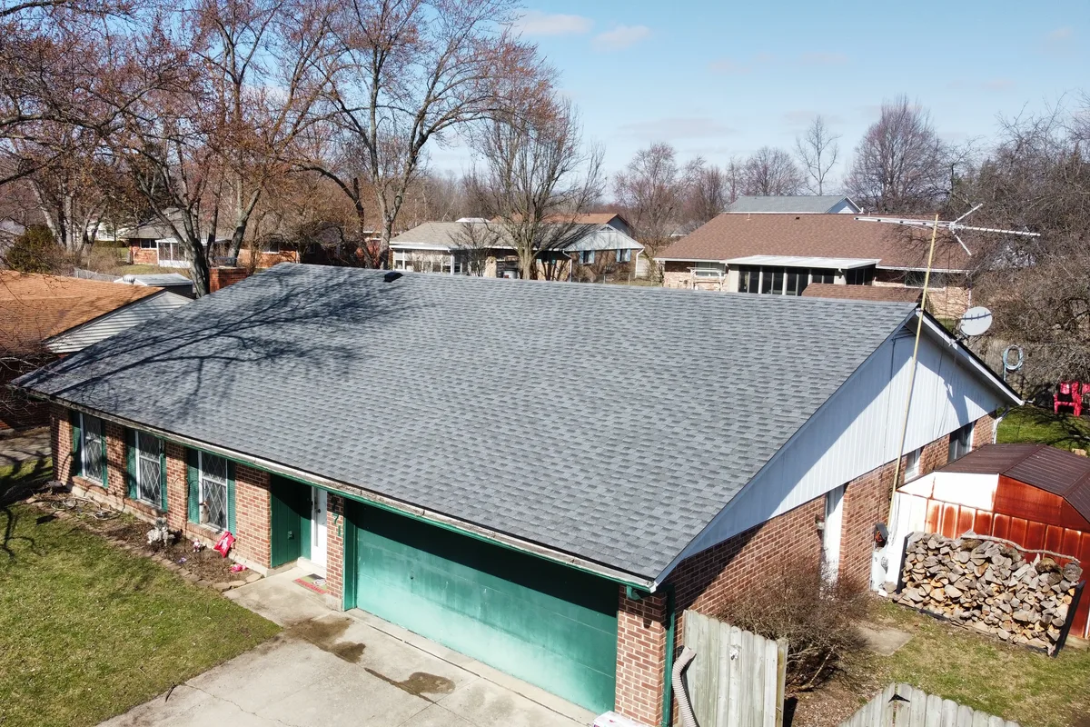 Drone view of a brick ranch on a residential street with a new charcoal shingle roof