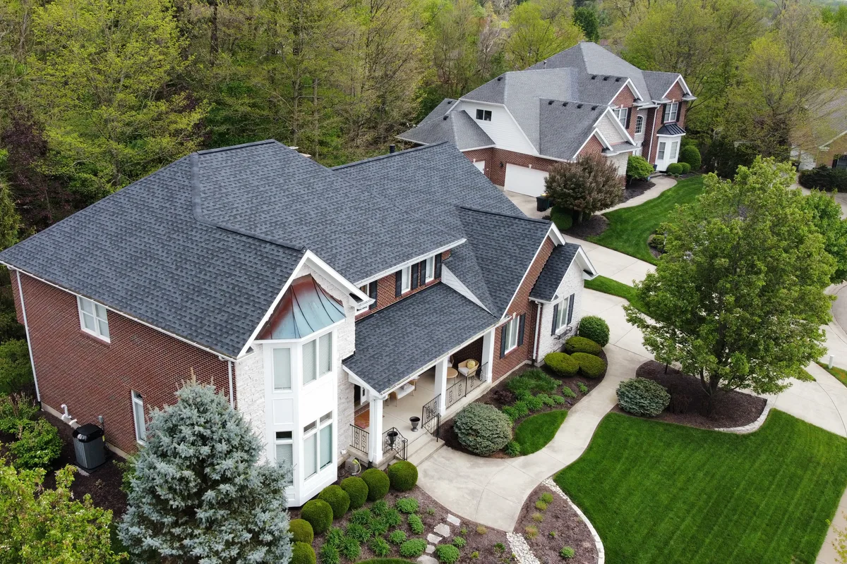 Aerial view of a large brick home with a new charcoal shingle roof and multiple gables