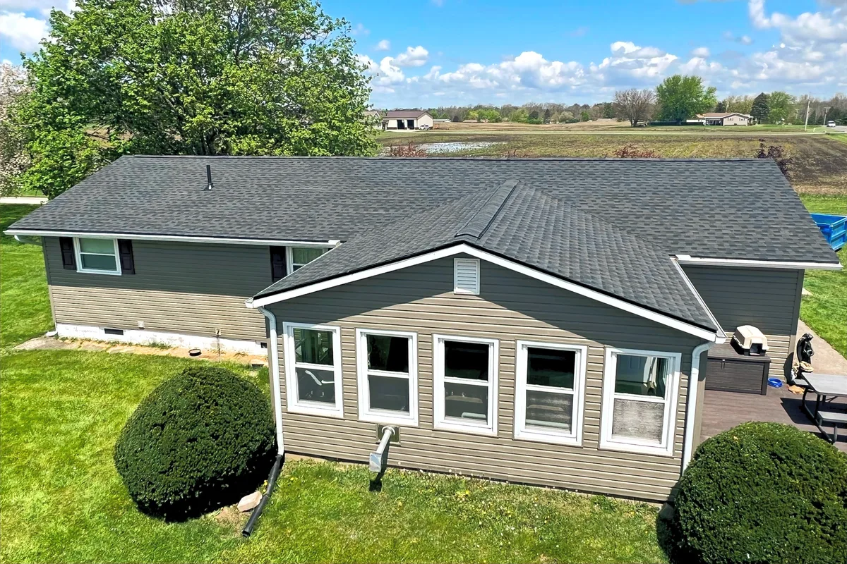 A ranch home with a new charcoal shingle roof beside a pond