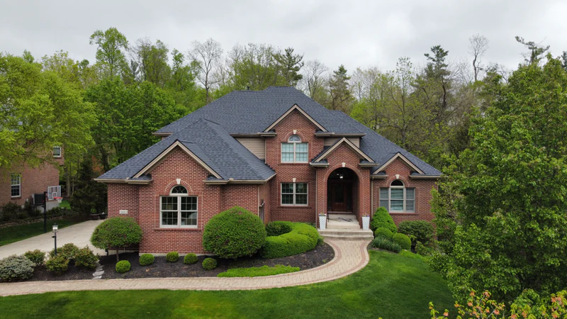 Aerial view of a brick one-story home with a new charcoal shingle roof and manicured landscaping