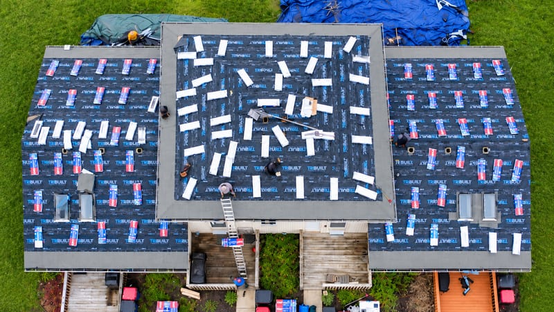 A SimpliRoofs crew laying asphalt shingles over fresh underlayment, from above