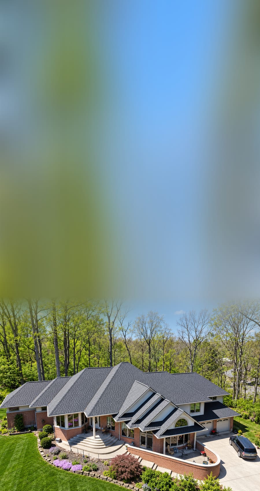 Aerial view of a brick ranch home in a wooded lot with a newly installed charcoal architectural shingle roof