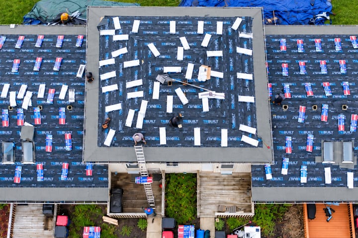Aerial view of a SimpliRoofs crew laying asphalt shingles over fresh underlayment, with bundles staged across the roof