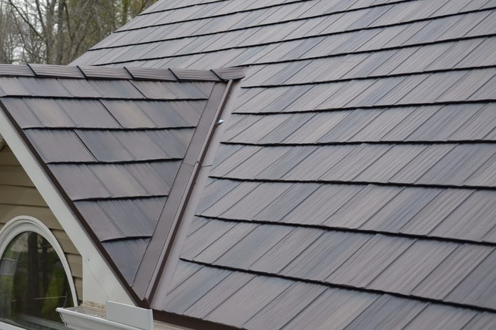 A metal shake roof in weathered brown and grey over a gabled dormer with an arched window