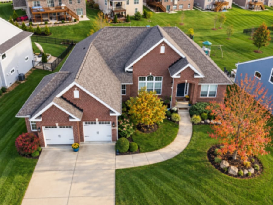 Aerial view of a brick home with a new shingle roof among autumn trees