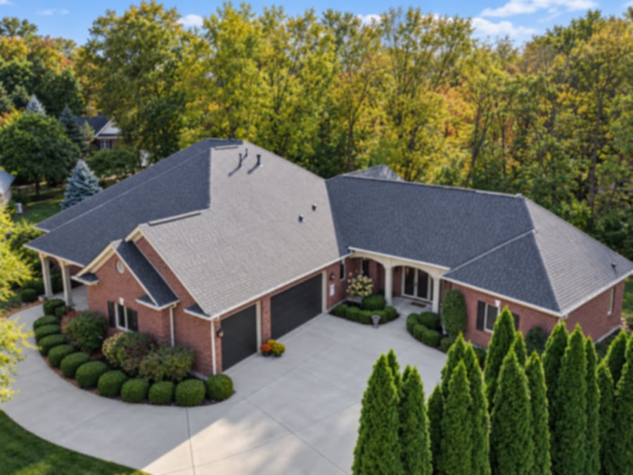 Aerial view of a brick ranch with a new charcoal shingle roof and a row of arborvitae
