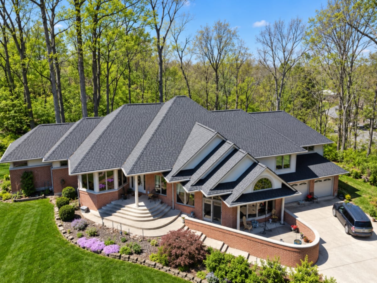 Aerial view of a long brick one-story home with a new charcoal architectural shingle roof, gabled windows and a curved brick patio wall