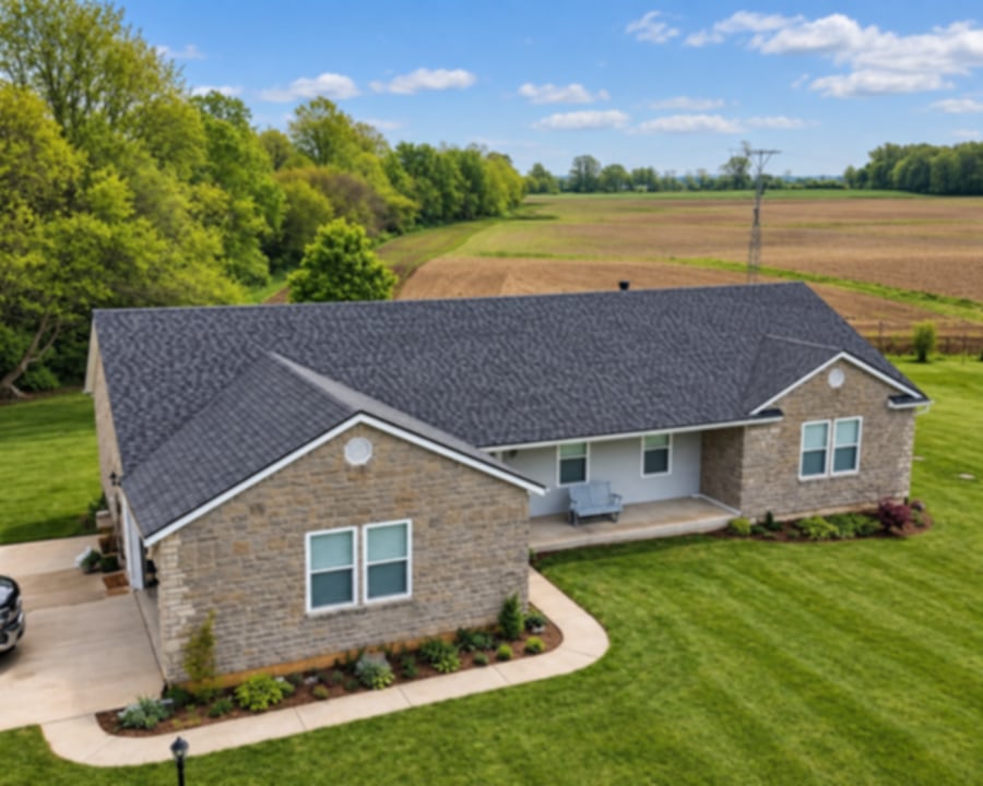 Aerial view of a stone ranch with a new charcoal shingle roof beside open farmland